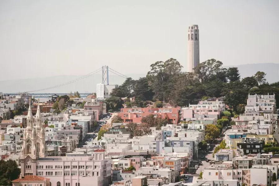 サンフランシスコのコイトタワーは、背景にベイブリッジ、前景に家々で覆われた丘を背景に描かれています。